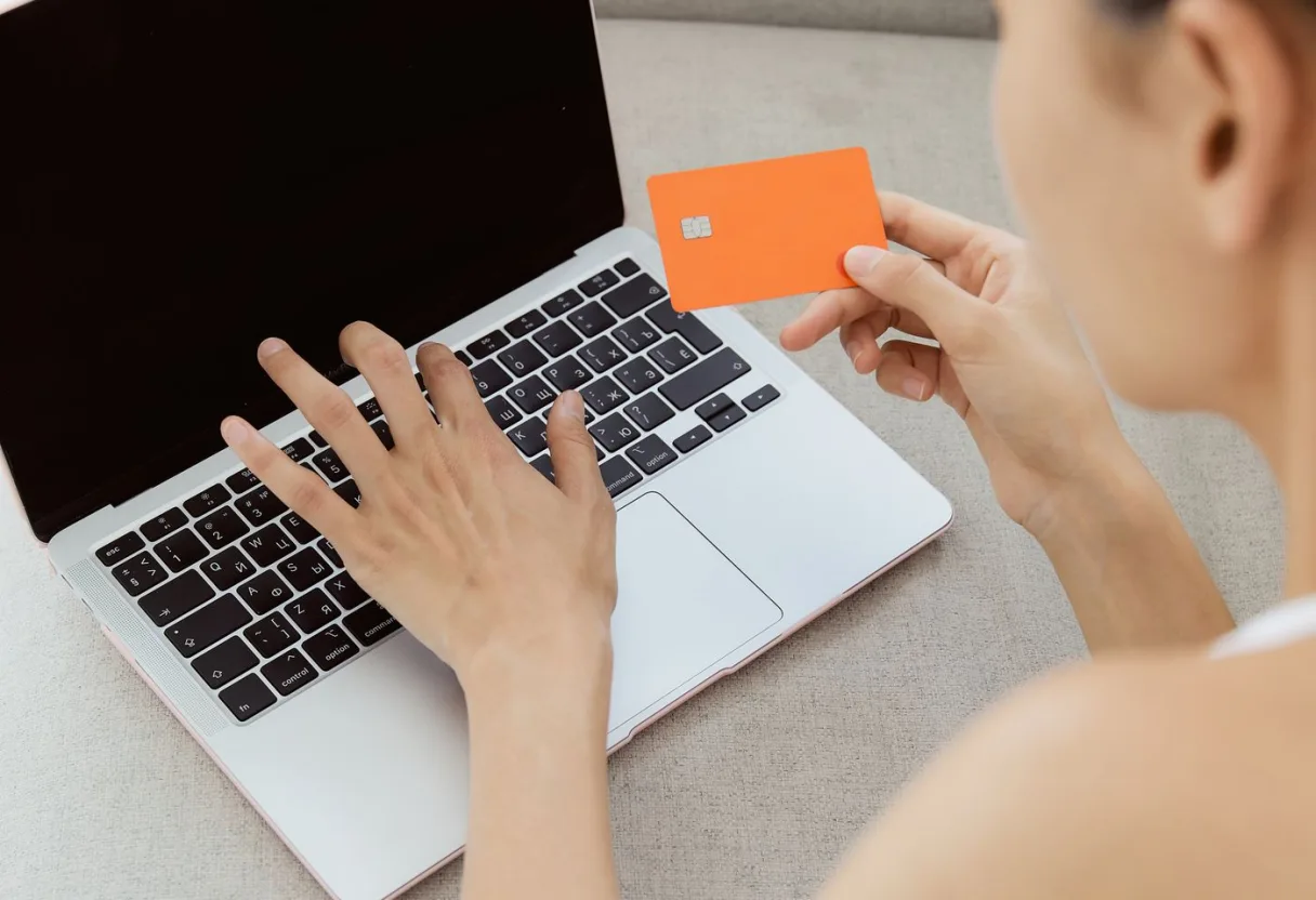 Kobieta z kartą bankową przy laptopie – przeniesienie IKE lub IKZE do innej instytucji